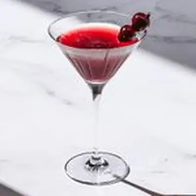 red-hued Cherry Bulldog cocktail in a cocktail glass, garnished with two skewered cherries