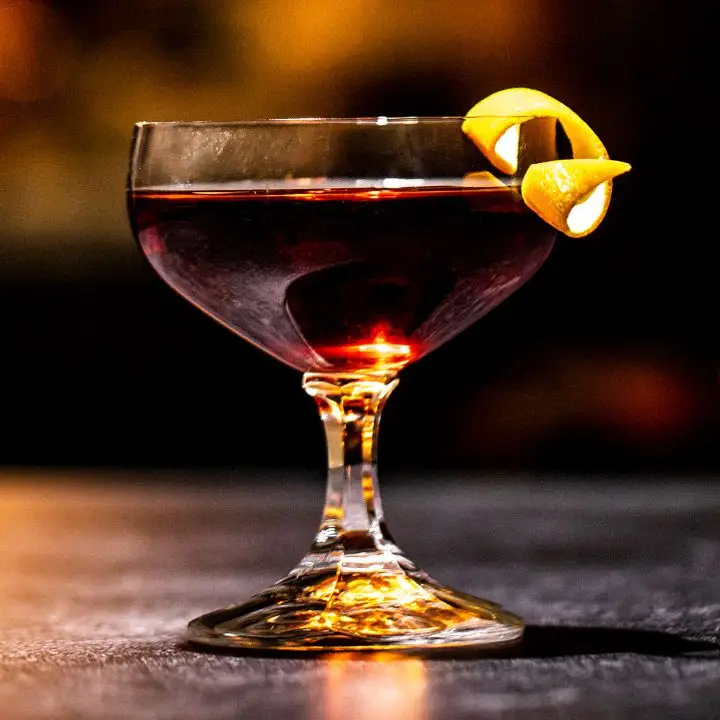 burgundy-colored Princess Mary’s Pride cocktail in a short-stemmed cocktail glass, garnished with an orange twist