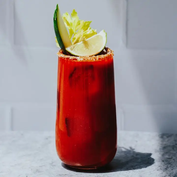Deep red Bloody Caesar cocktail with lime and celery garnishes