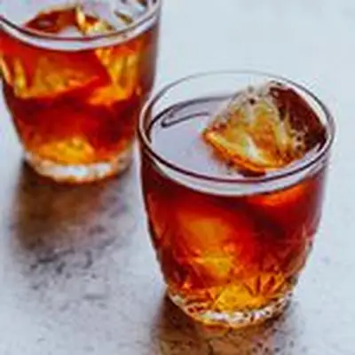 Two rocks glasses with star-like designs hold a crimson drink over a few large ice cubes. They’re dusted with nutmeg. 