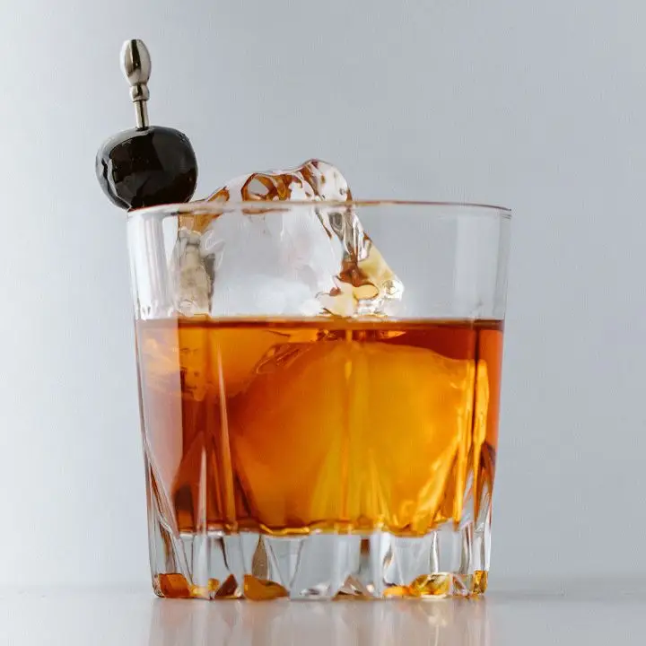 Full Monte cocktail in a rocks glass with two large, clear ice cubes and a skewered cherry garnish