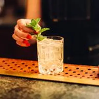A hand with red nails garnishes a clear drink (A Rake