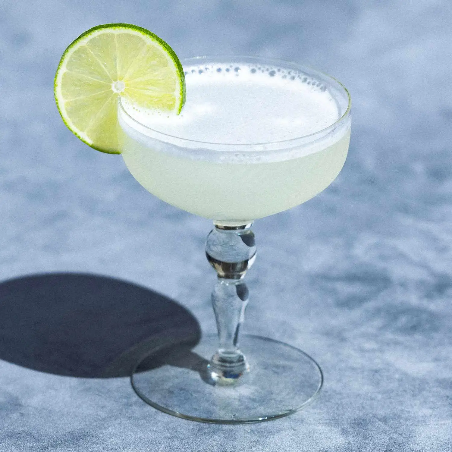 Classic Gimlet cocktail, pale green, in an old-fashioned coupe glass, garnished with a lime wheel