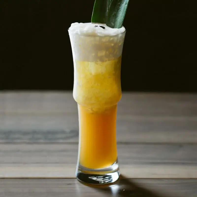 A Lonely Island Lost in the Middle of a Foggy Sea in a collins glass, with foamy top, garnished with coffee beans and pineapple fronds