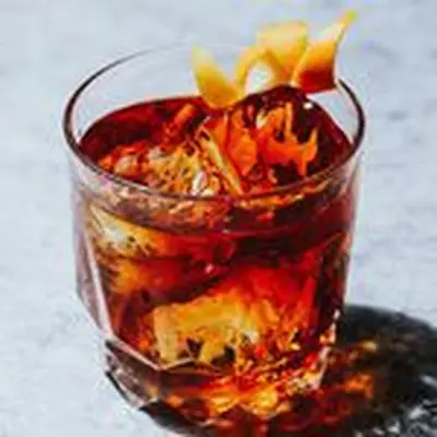 Tender Nob stirred brown cocktail with two ice cubes and orange twist in rocks glass, set on marble surface 