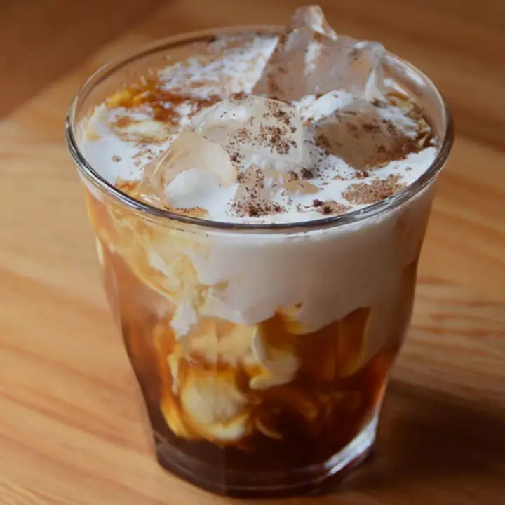 Espresso Milk Punch in a rocks glass with ice, cream and ground espresso on top