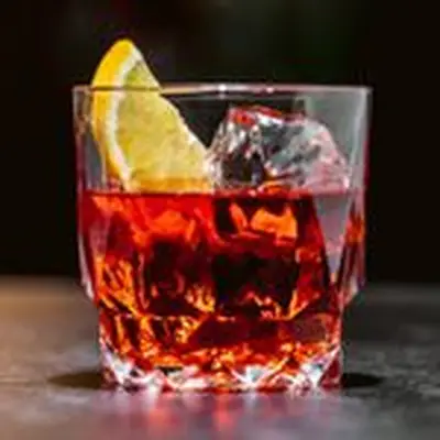 A beveled rocks glass with clear ice, a ruby-red Negroni, and an orange half-slice
