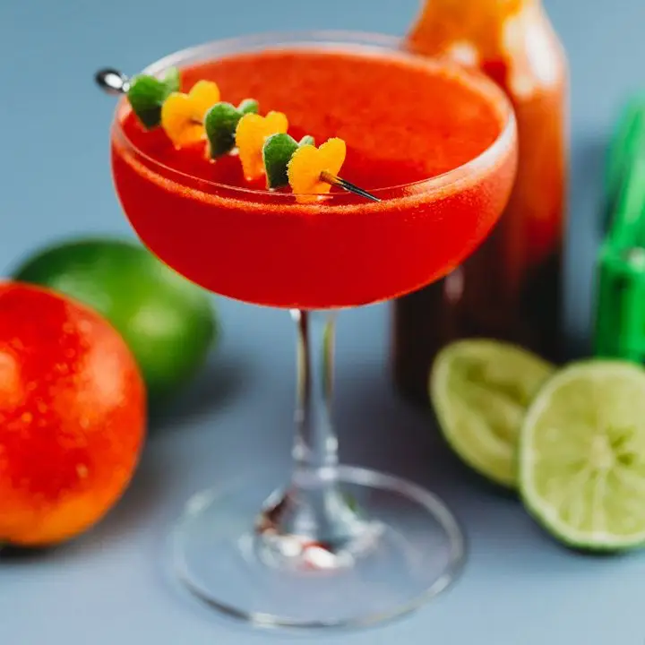 red-hued Hot Blooded cocktail in a coupe glass, garnished with heart-shaped orange peels and lime peels on a skewer