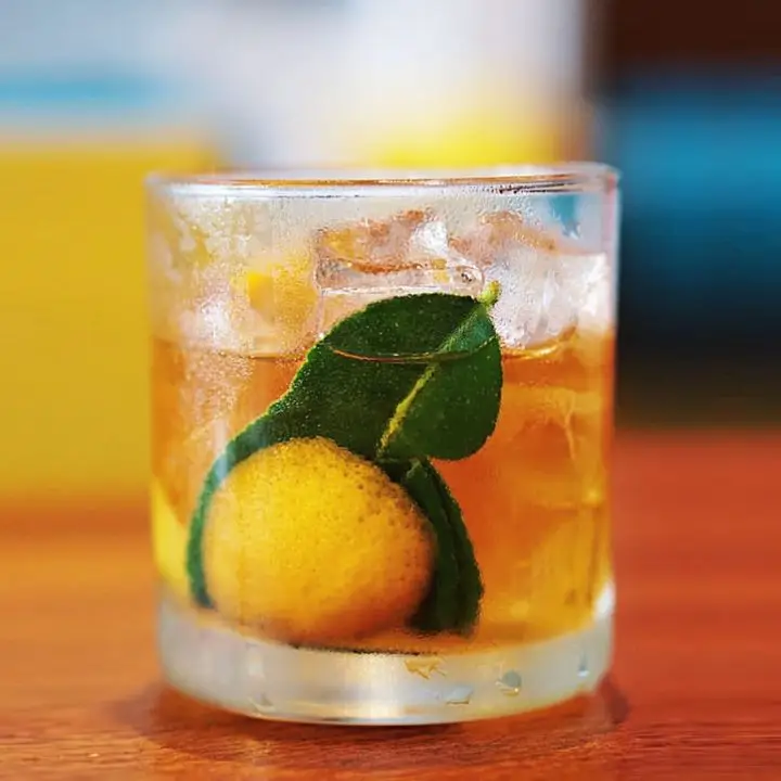 A rocks glass holds an Old Fashioned with ice, lime leaves and a lemon zest.