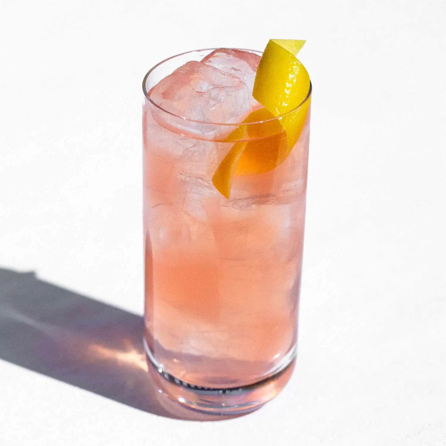 Pink Lone Ranger cocktail served in highball glass with cubed ice and lemon twist, shot against white background