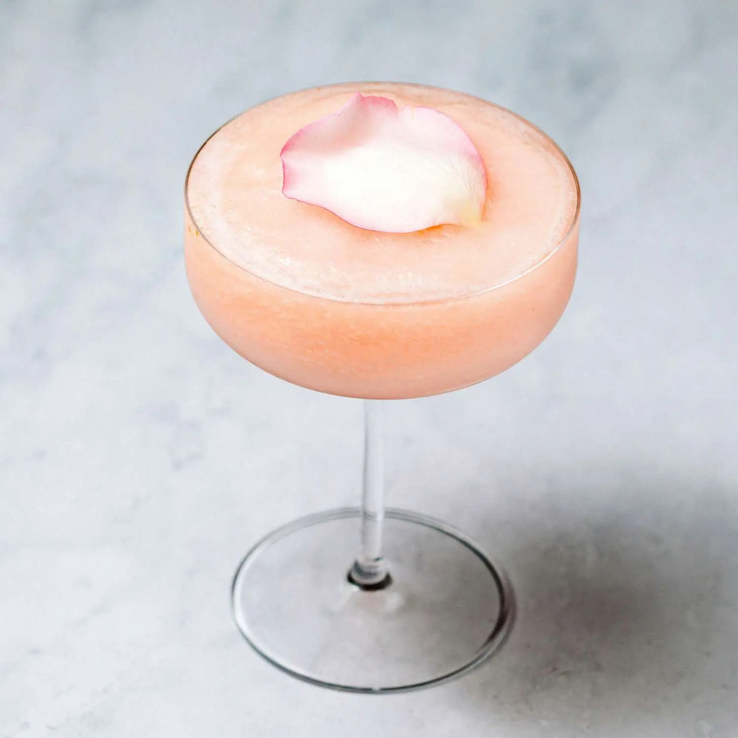 Pink and frozen Guava Rose cocktail served in coupe glass and garnished with pink rose petal, shot against marble backdrop