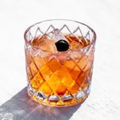 Anejo Tequila Old Fashioned in rocks glass with engraved diamond pattern with cherry garnish, on white background