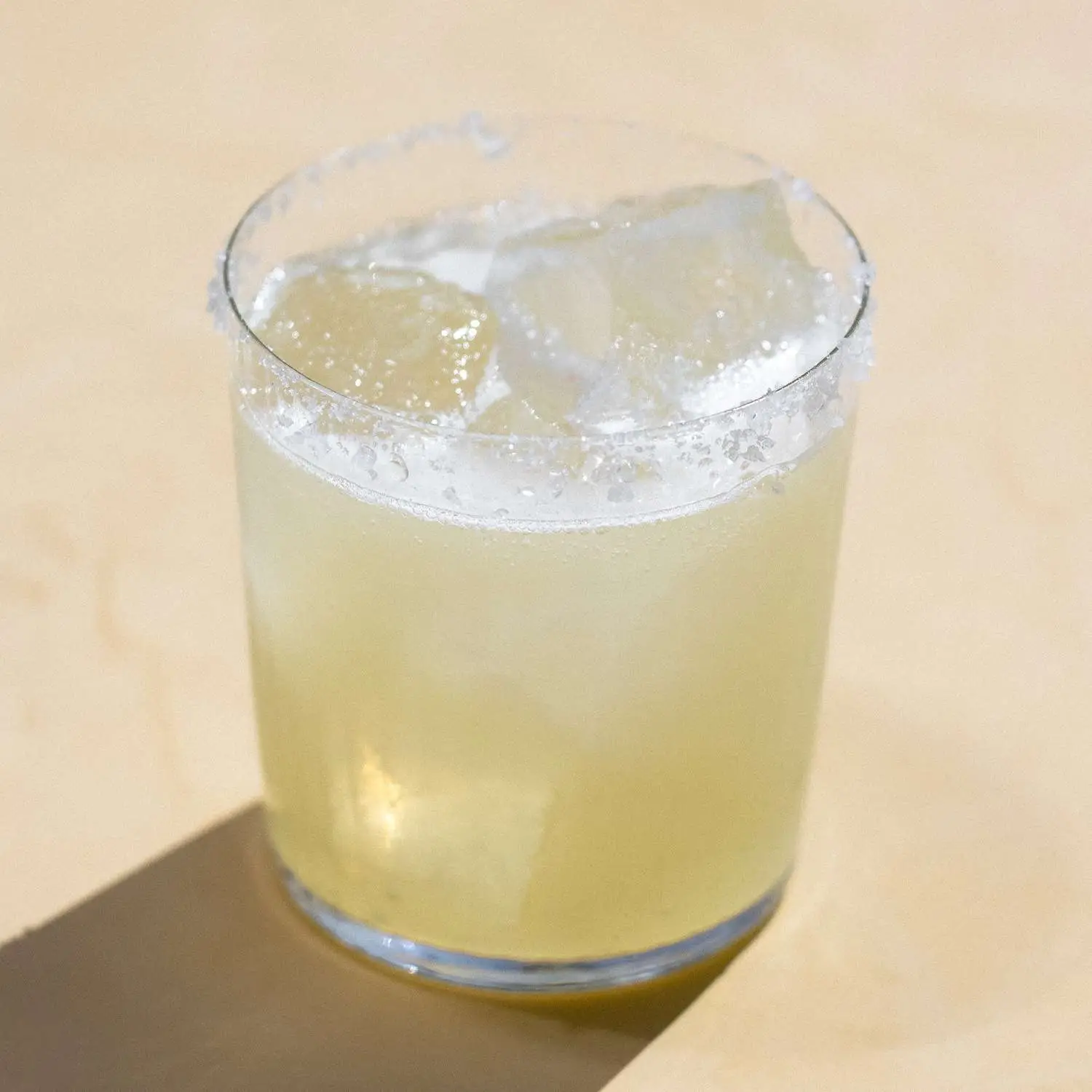 Tommys Margarita served in rocks glass with salt rim, shot against tan background