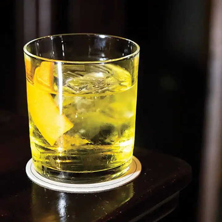 bright yellow white negroni cocktail on a dark bar