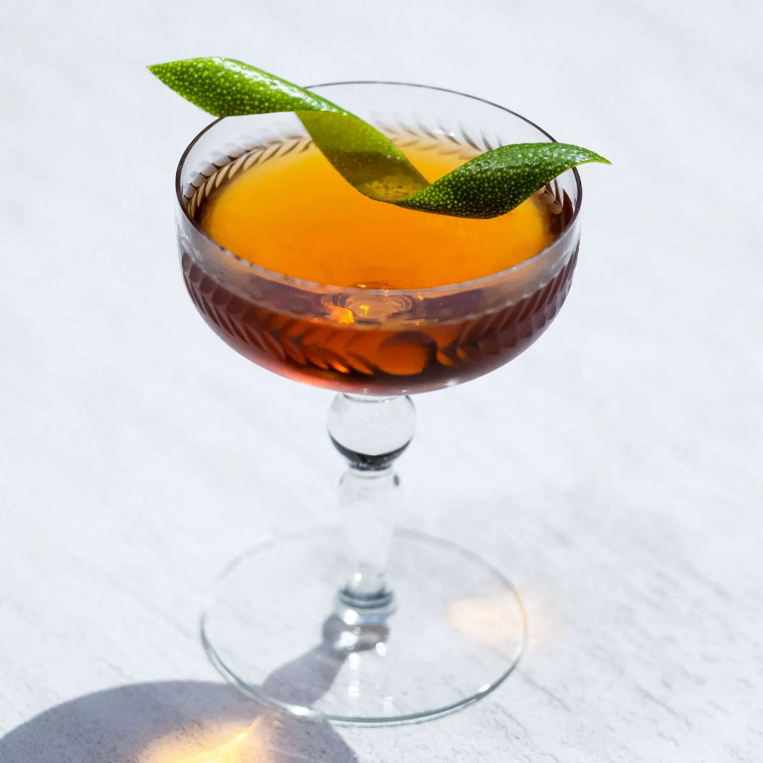 Tequila Manhattan cocktail served in a coupe and garnished with lime twist, shot against marble background