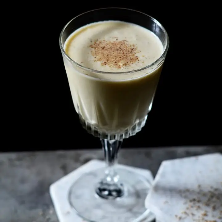 spiced eggnog cocktail in a wine glass with fresh nutmeg on top