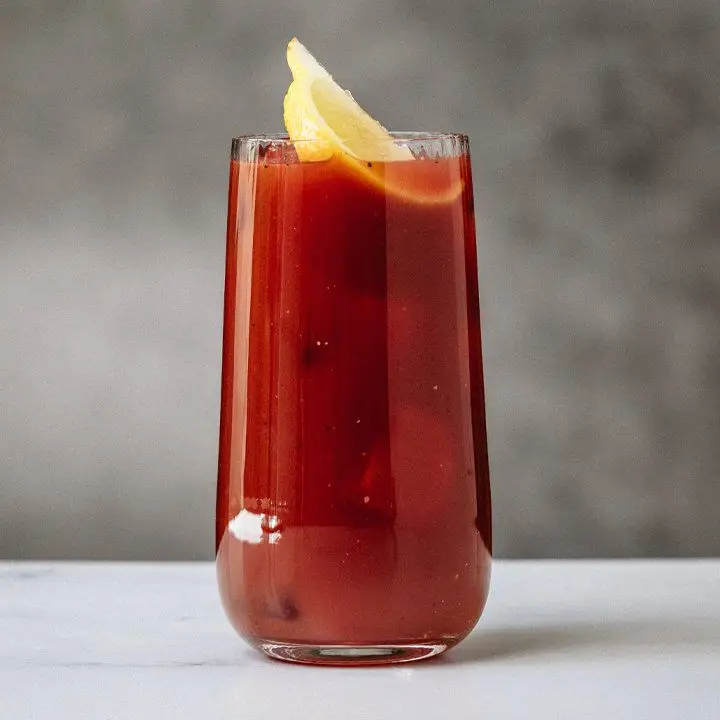 red-colored Bloody Bull cocktail in a collins glass with a lemon wedge garnish