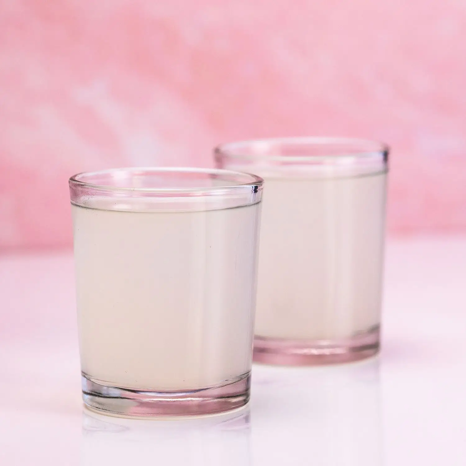 Two pale green Kamikaze drinks in shot glasses, on light pink background