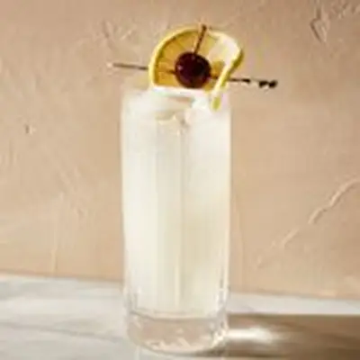 Tom Collins cocktail in highball glass garnished with lemon wheel wrapped around a maraschino cherry on a cocktail skewer