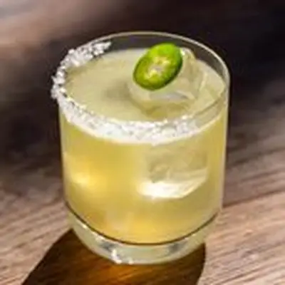 Spicy Margarita in ice-filled rocks glass with half salt rim and jalapeno coin garnish, shot on wooden surface