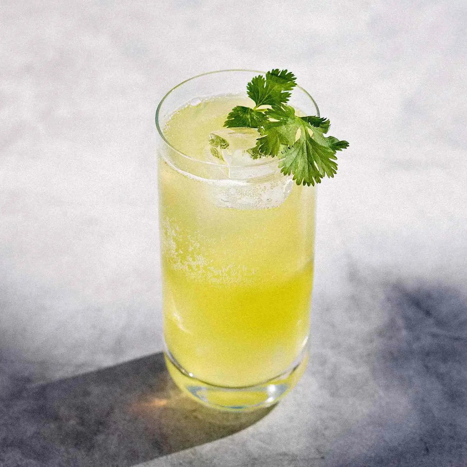 Tequila Limeade, bright greenish-yellow, in highball glass with fresh mint sprig, on marble background