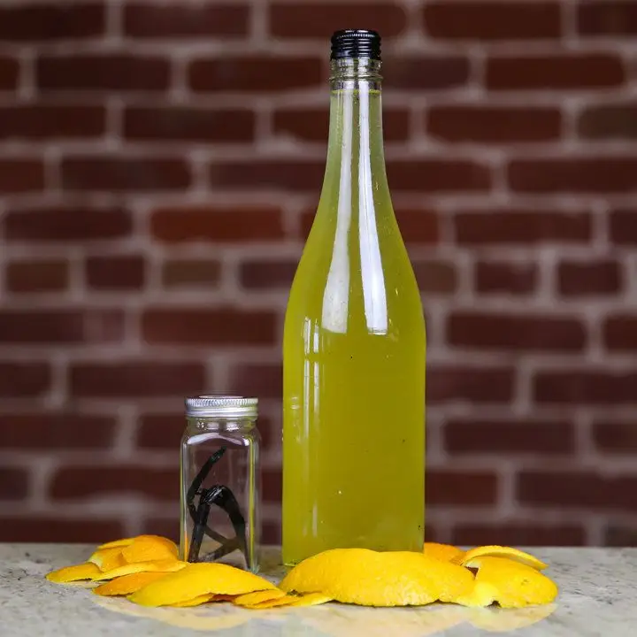 A bottle of homemade vanilla-orangecello next to a small jar of vanilla beans and a handful of orange peels