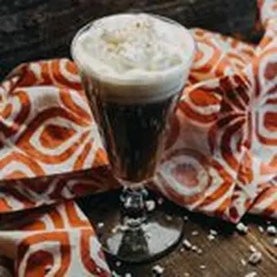 Gran Rosta Coffee cocktail in an Irish Coffee mug with whipped cream topping, served next to orange-and-white towel