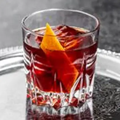 A crimson-hued Negroni on a large ice cube in a chunky rocks glass rests on a silver platter.