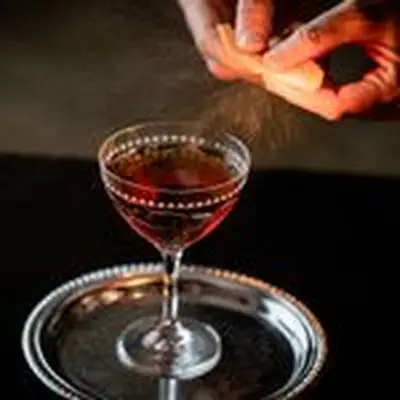 Hands express orange peel oils over the top of the Longshoreman cocktail