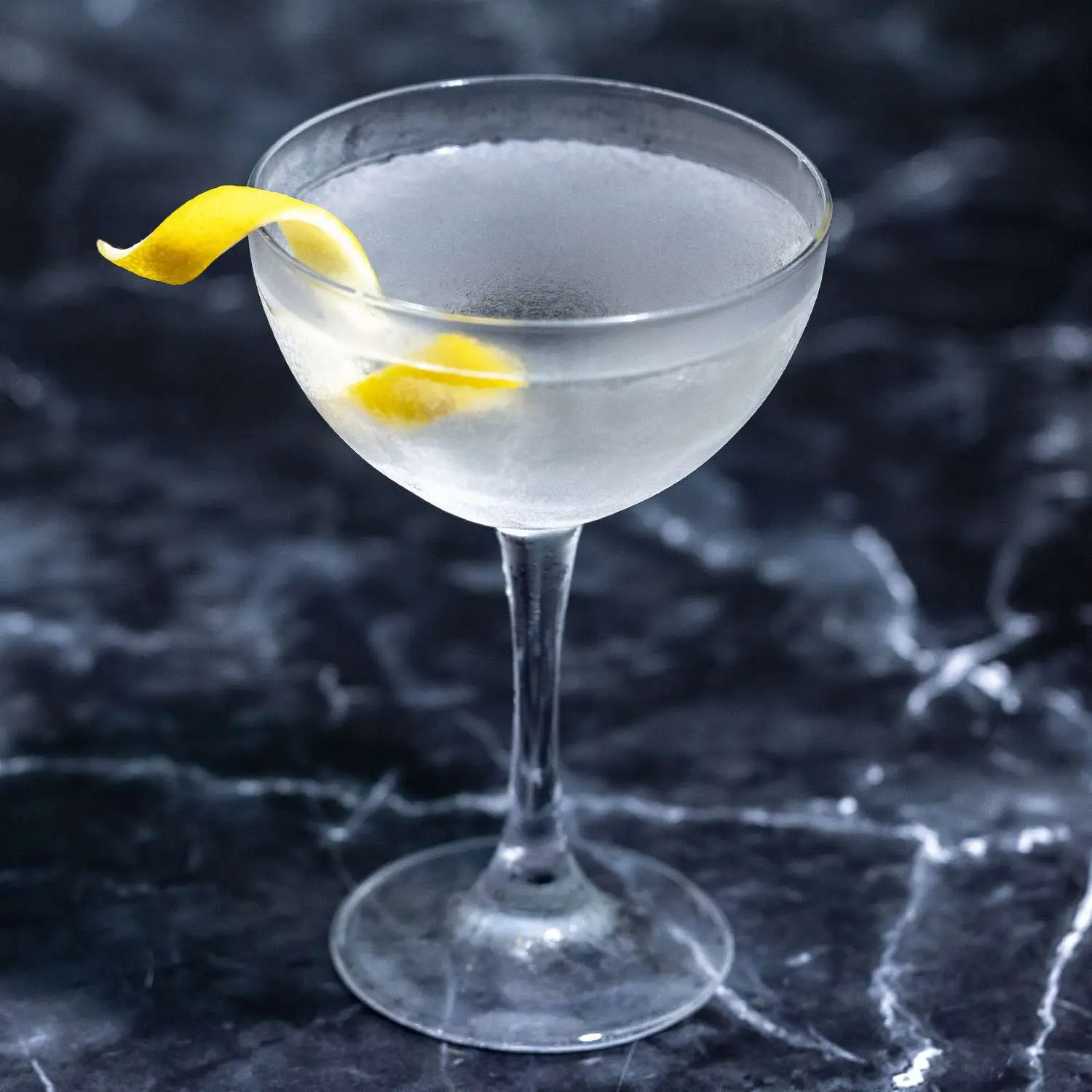 Vesper Martini in a throwback coupe glass with lemon twist, on dark marble background