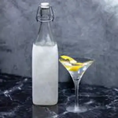 A frozen flip-top bottle filled with gin, standing next to a v-shaped Martini glass showing a Dukes Martini with a lemon twist