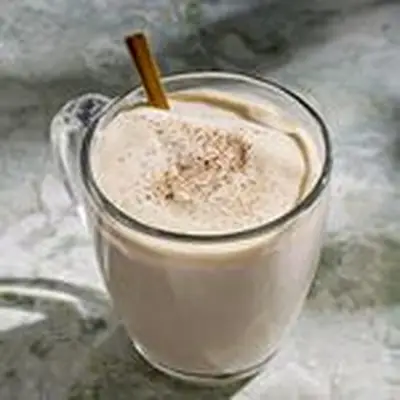 Tom & Jerry cocktail in clear coffee mug with metal spoon and dusting of ground clove, nutmeg, and allspice on top