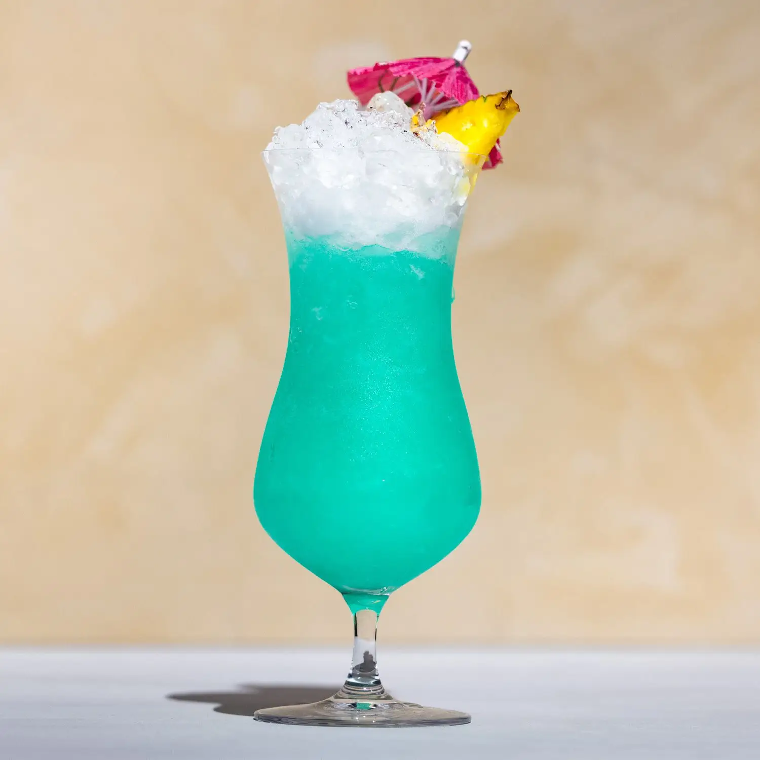 Blue Hawaii cocktail, bright teal and served over crushed ice in a curved Hurricane glass, garnished with a pineapple wedge and miniature red umbrella