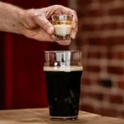 hand holding a shot glass over a pint of Guinness to make an Irish Shot