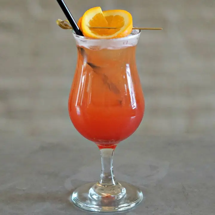 A red-hued Spritz in a hurricane glass, garnished with an orange wheel on a pick