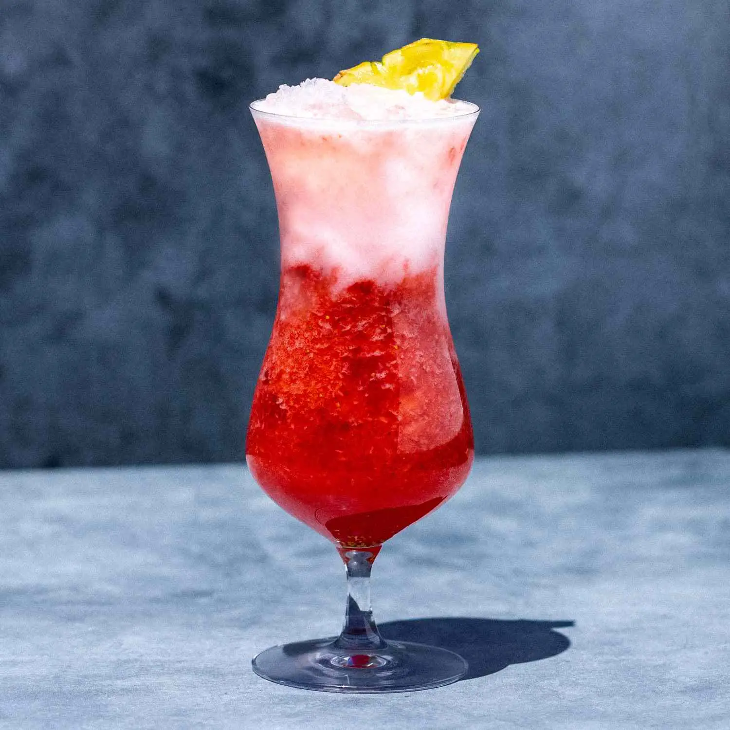Miami Vice cocktail in curved Hurricane Glass, with white Pina Colada layer floating on top of red Strawberry Daiquiri layer, and pineapple wedge garnish