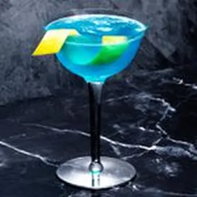 An elegant coupe with a tapered rim sits on black marble. It holds a vivid blue cocktail garnished with a twisted lemon peel.