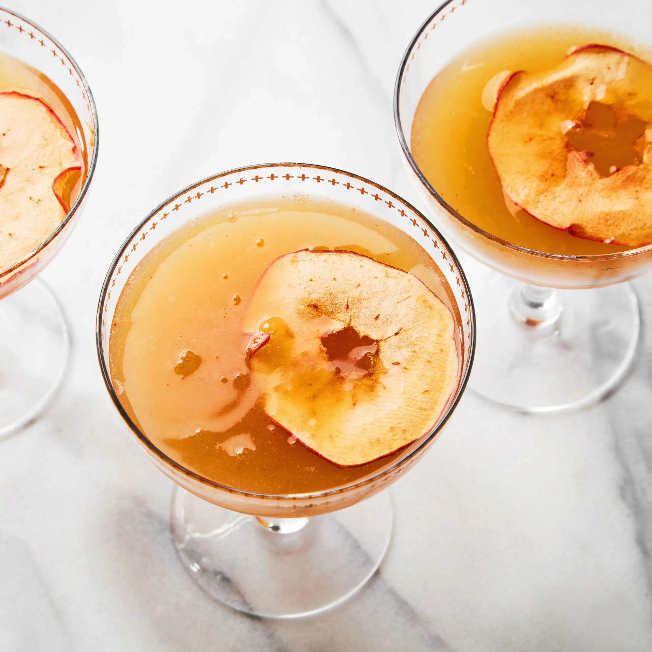 3 Paradise Apple Thanksgiving cocktails in coupes with apple garnish.