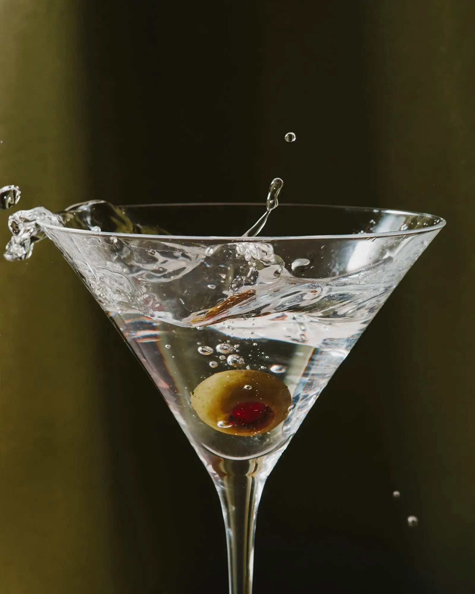 An olive being splashed into a Vodka Martini.