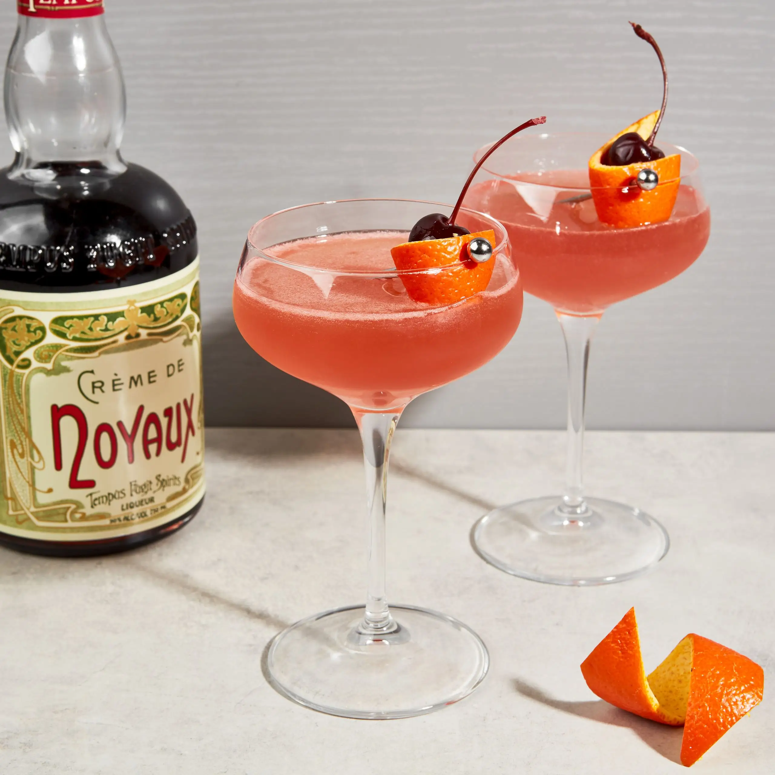 Two coupe glasses with King Kong cocktails garnished with orange twists and cherries.