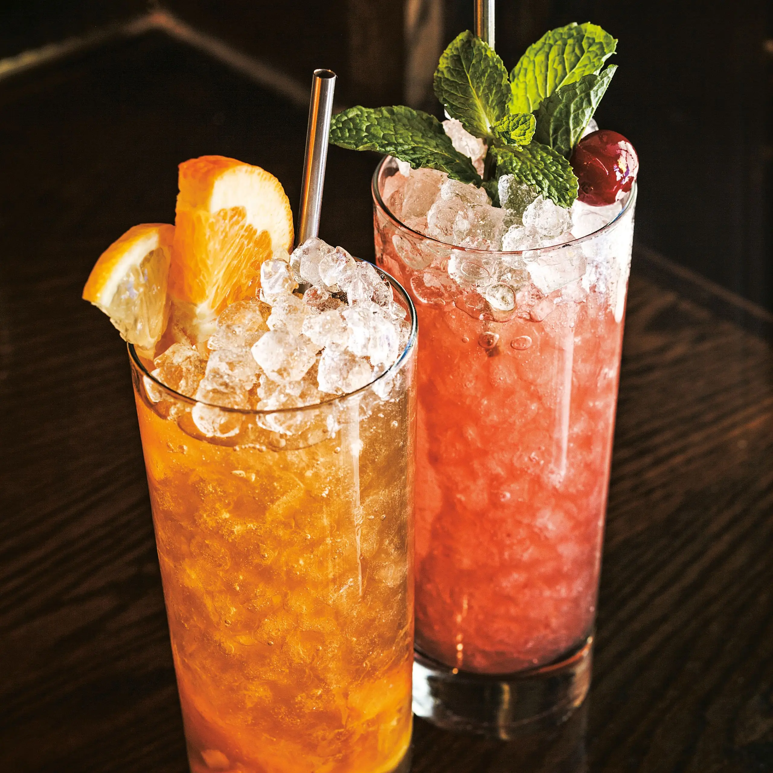 Photo of two sherry cobblers in tall glasses with crushed ice or pebbled ice and metal straws.