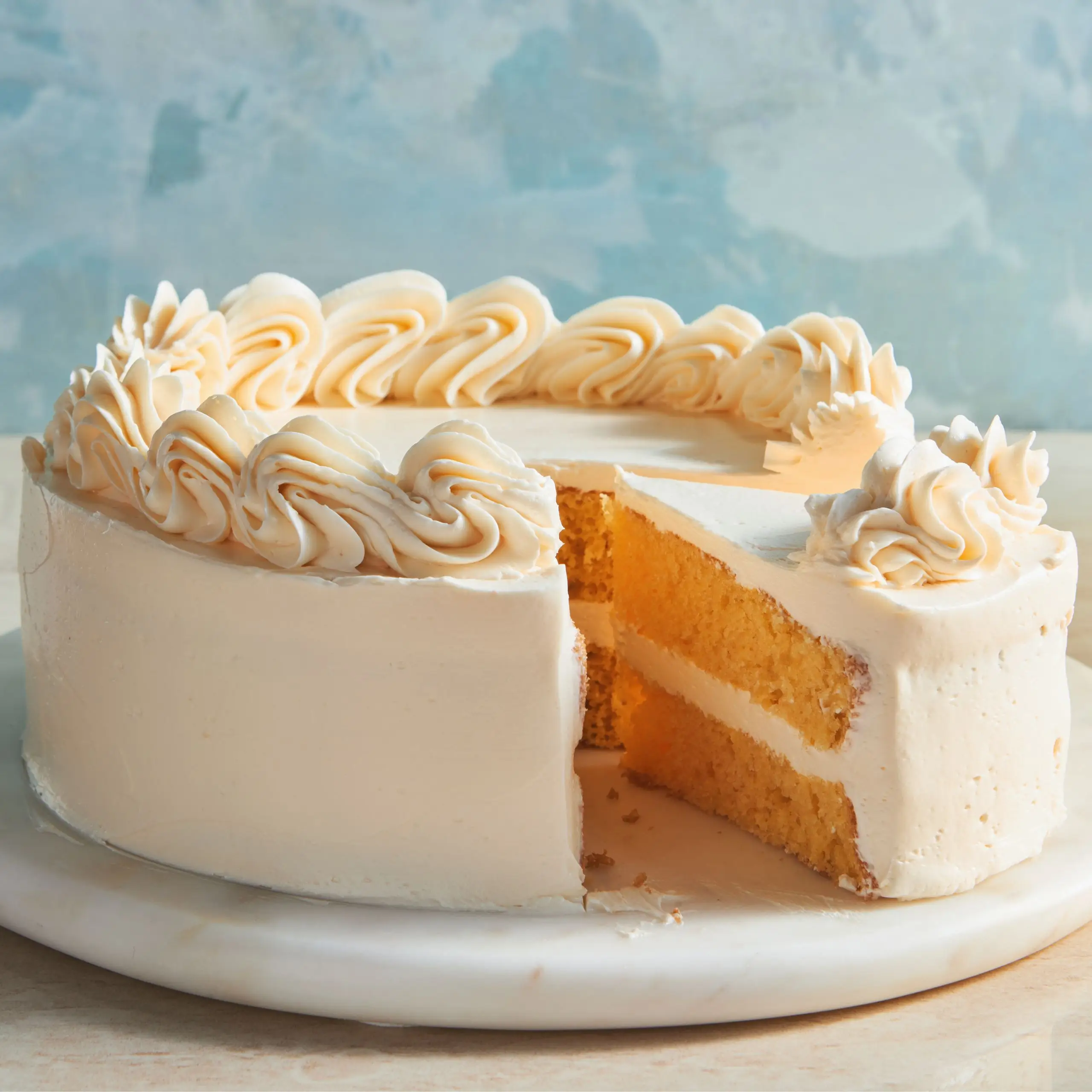 A vanilla cake frosted with Italian Meringue Buttercream with a slice removed.