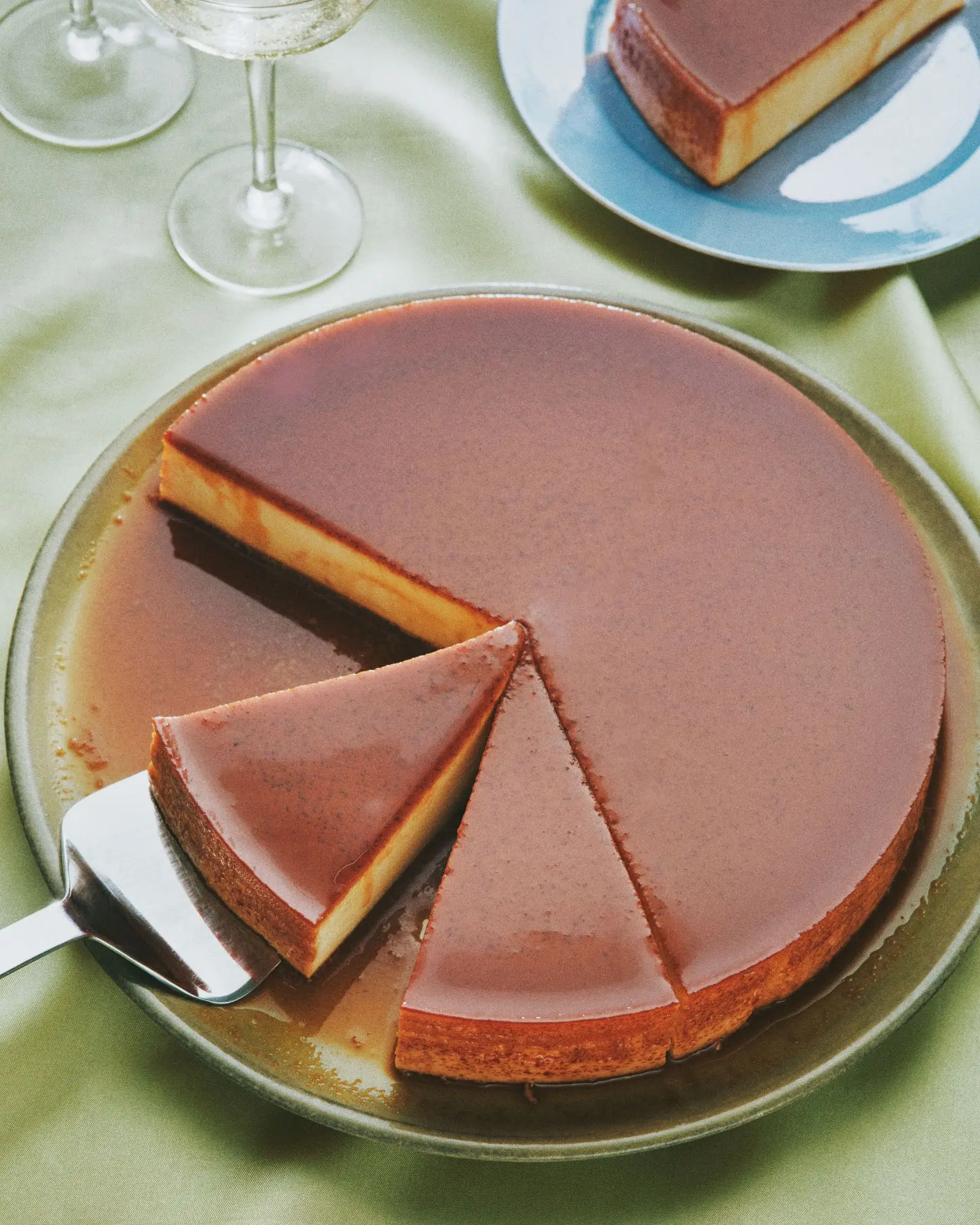 Flan de queso on a cake plate with three slices cut out.