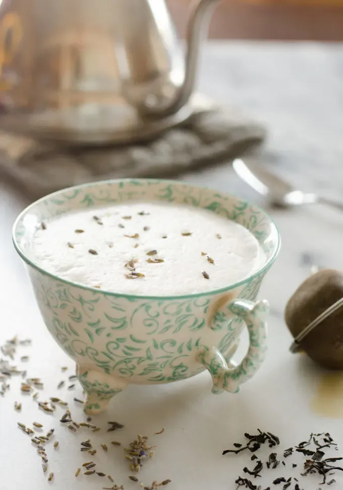 A teacup filled with a London Fog Tea Latte with a tea kettle in the background and a tea strainer off to the side.' title='Homemade London Fog Tea Latte (Earl Grey Latte)