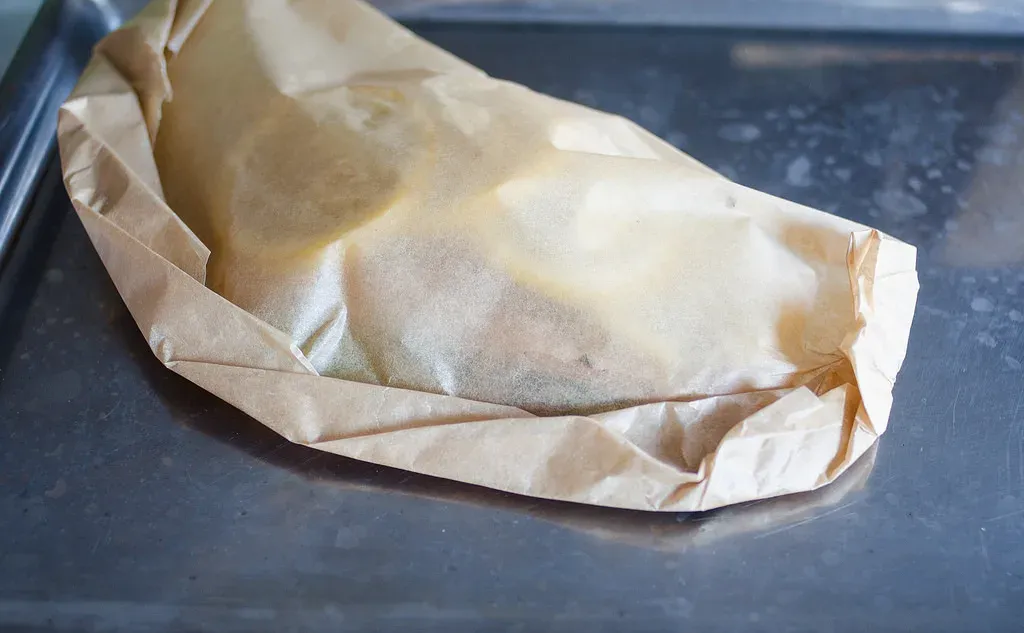 The salmon fillet on a baking sheet all wrapped up in a piece of parchment paper.' title='Salmon en Papillote