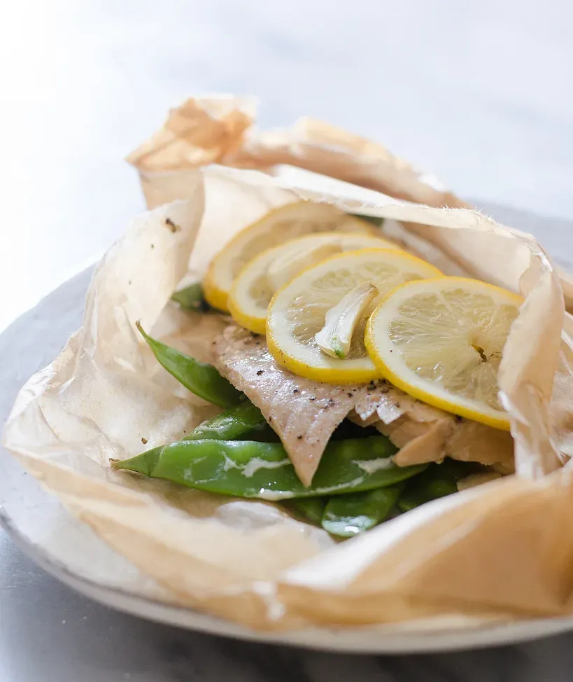 Salmon en Papillote: A salmon filet in a piece of parchment paper with snow peas underneath and slices of lemon on top.' title='Salmon en Papillote