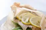 Salmon in a parchment paper packet with snow peas underneath and lemon slices on top.' title='Salmon en Papillote