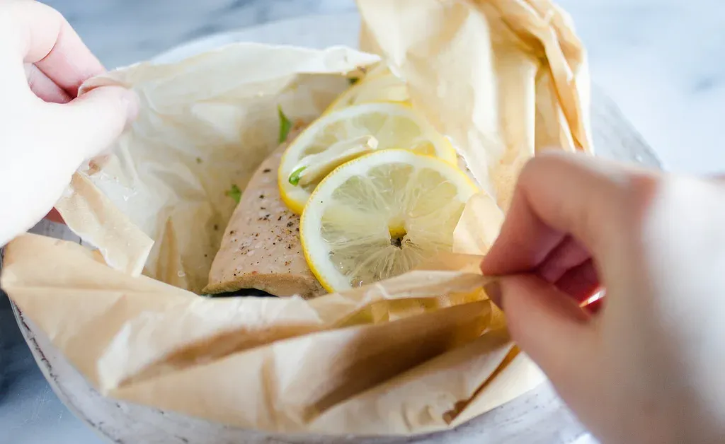 Salmon en Papillote: A salmon filet in a piece of parchment paper with snow peas underneath and slices of lemon on top.' title='Salmon en Papillote