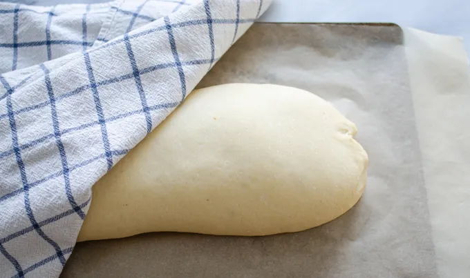 The risen loaf of bread with a tea towel partially covering it. ' title='Soft Sourdough French Bread Without Yeast!
