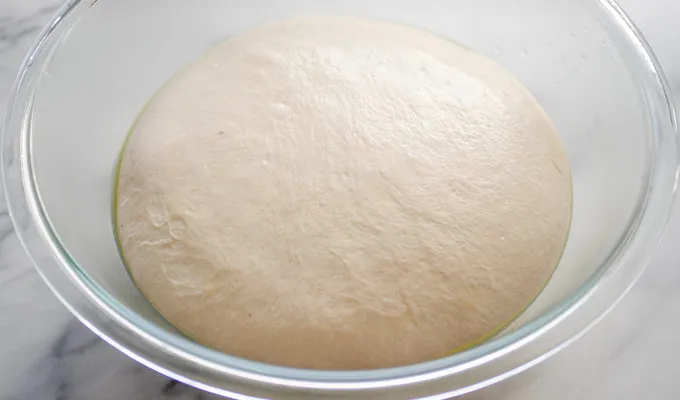 The risen sourdough french bread dough in a large bowl on a marble surface.' title='Soft Sourdough French Bread Without Yeast!